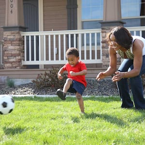 Boy playing soccer with mom in the front yard